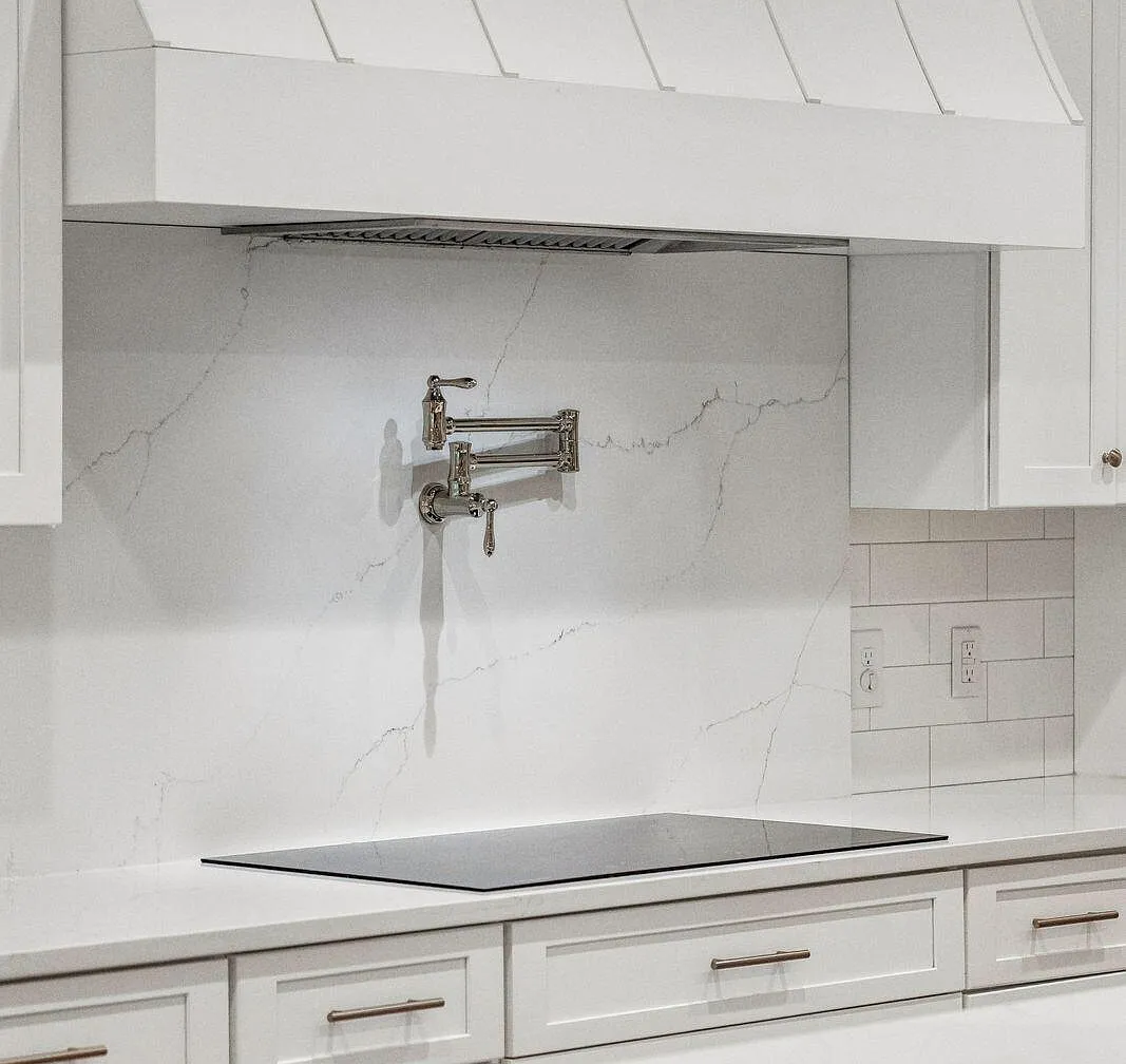 Detail of the kitchen cooktop wall: a custom white panel hood above a brushed nickel articulating pot-filler faucet, a single induction cooktop, and a veined marble slab backsplash